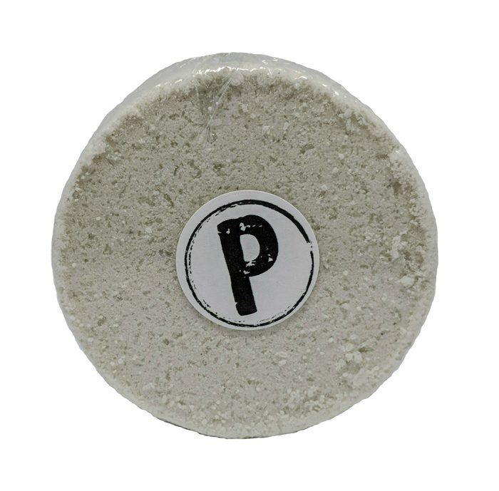 A round white bath bomb stamped with the shop's circled P mark