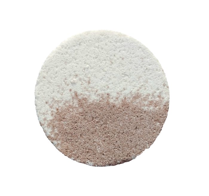 A round bath bomb with a white half and a dusty pink half